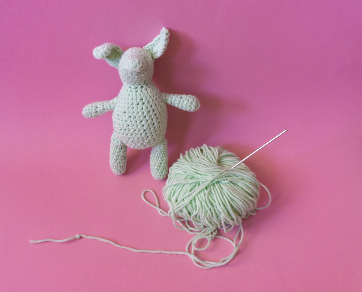 Coelhinho de amigurumi em crochê ao lado de um novelo de fio verde-claro com agulha