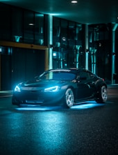 A modern car with dark tinted windows and vibrant LED lights parked in an urban setting at dusk.