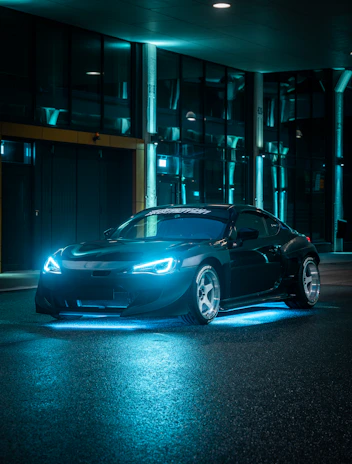 Cinematic shot of a sleek autonomous vehicle navigating through a smart city at night, illuminated by vibrant cyan and violet neon lights.