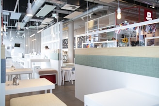 A bright, modern cafe interior with a wooden counter displaying colorful burgers and wraps.