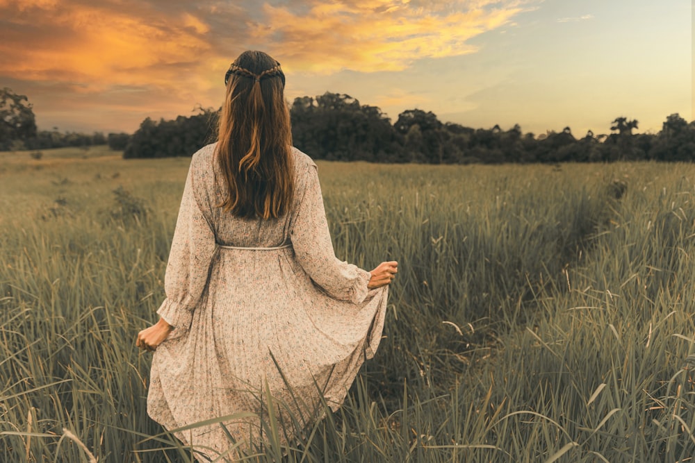 mulher no vestido branco da manga comprida em pé no campo verde da grama durante o pôr do sol