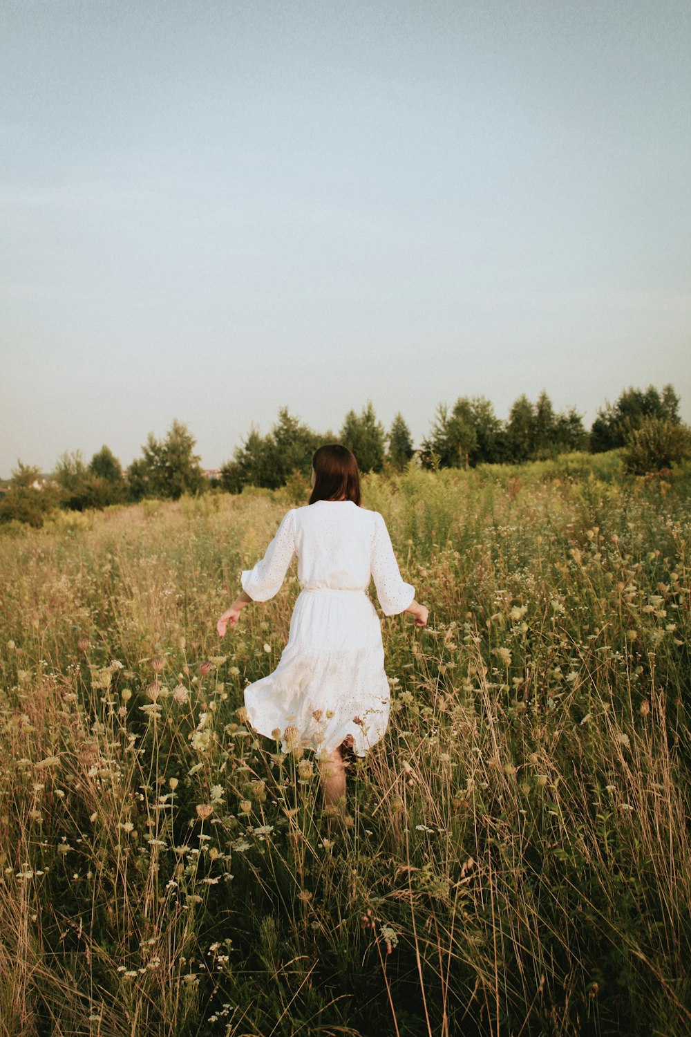 woman in white dress walking on green grass field during daytime