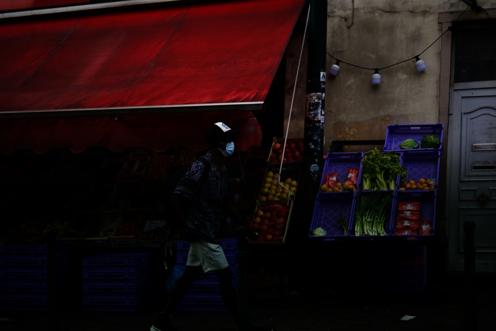 man in black and gray long sleeve shirt and blue denim jeans standing near fruit stand