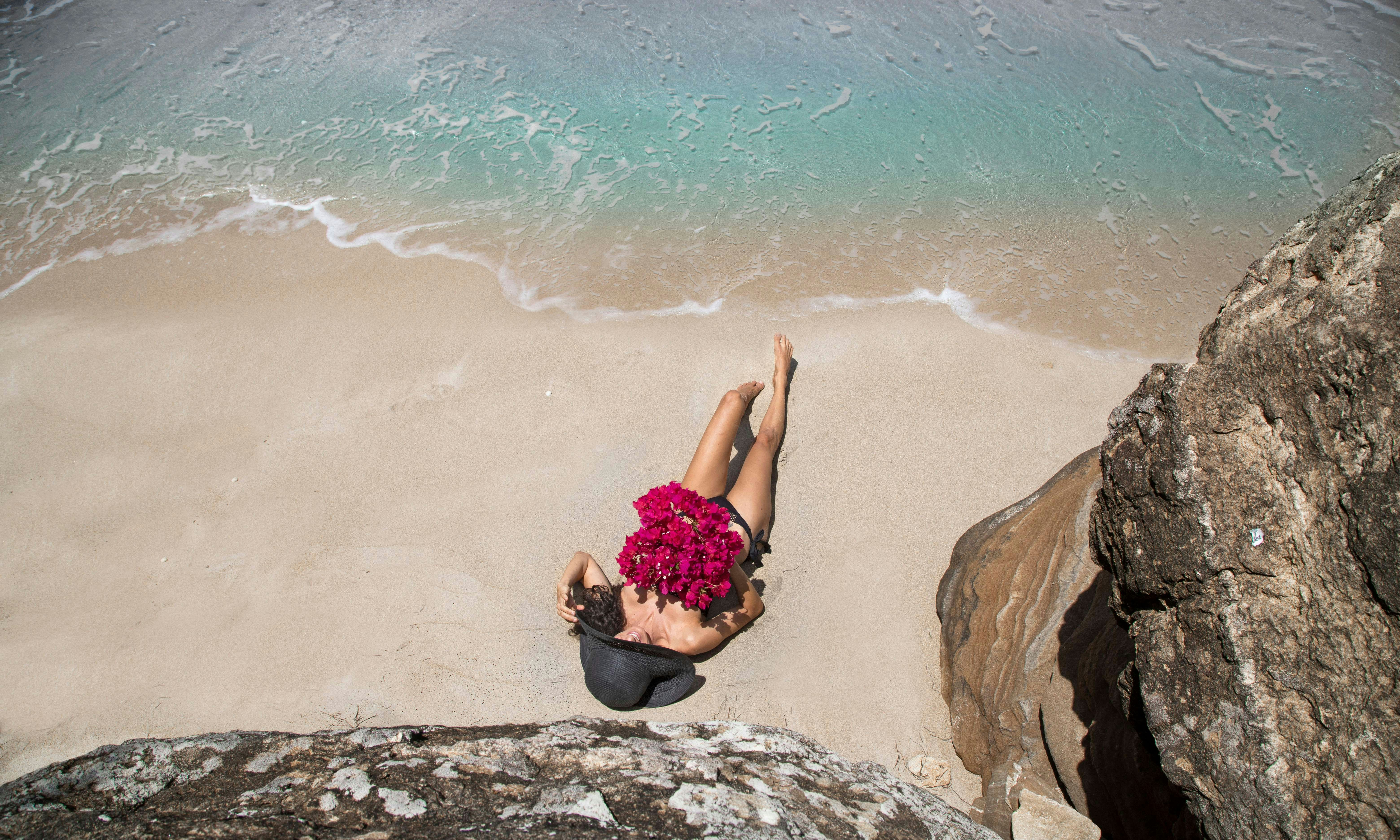 woman in black and pink floral dress sitting on brown rock near body of water during, 
