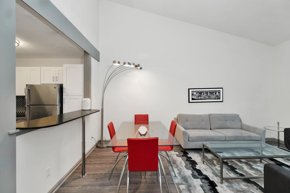 Modern living room with glass dining table, red chairs, and industrial black refrigerator