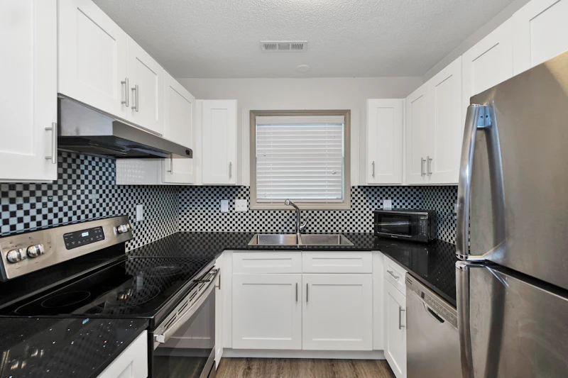 Modern kitchen with white cabinets, black granite countertops, checkered backsplash, and stainless steel appliances