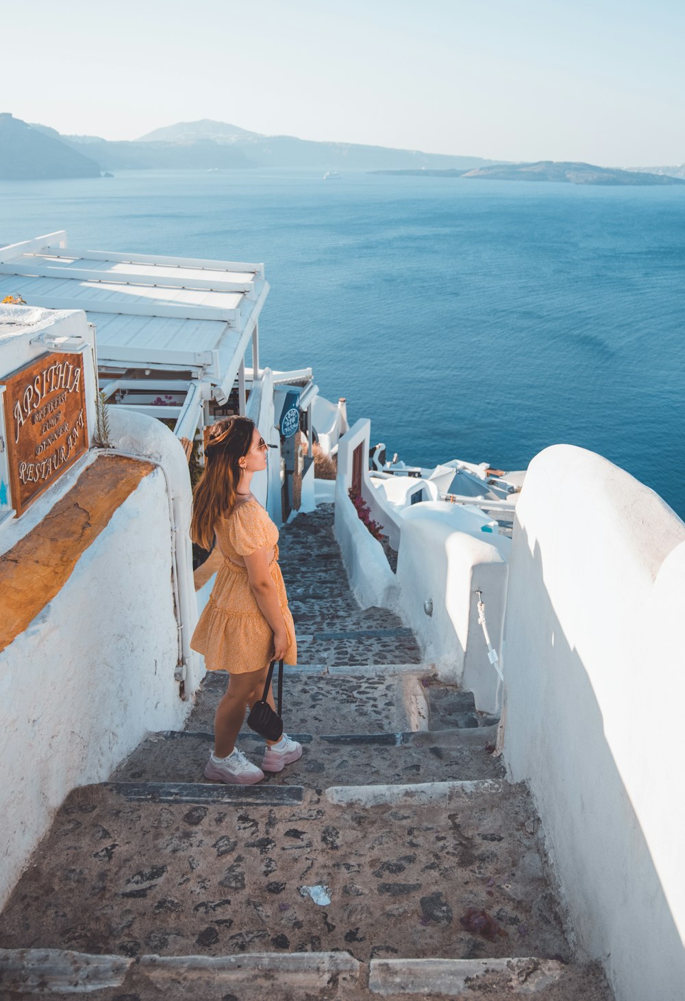 woman in orange dress standing on concrete wall near body of water during daytime