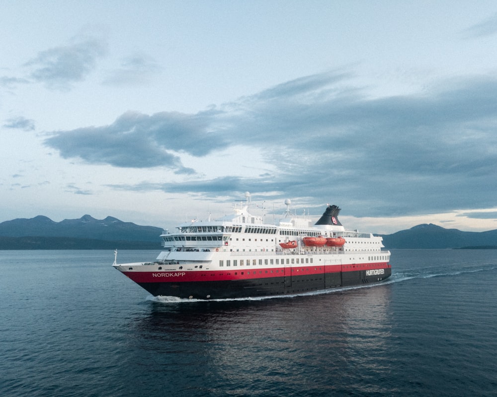 white and red cruise ship on sea under white clouds and blue sky during daytime