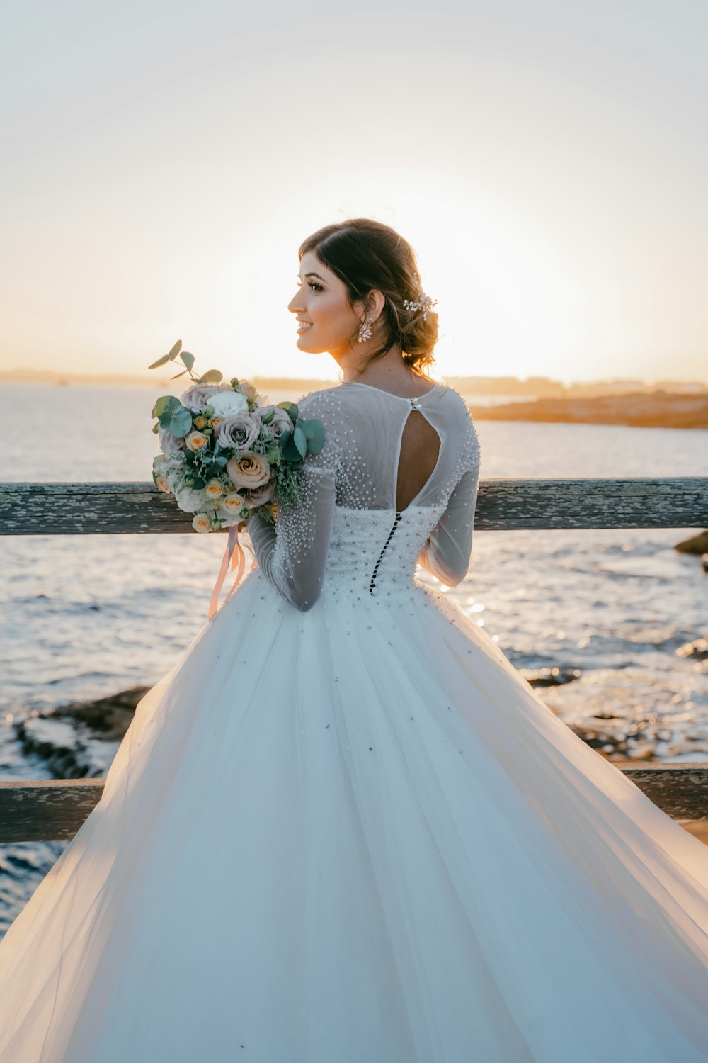 woman in white sleeveless dress holding bouquet of flowers standing on beach during sunset