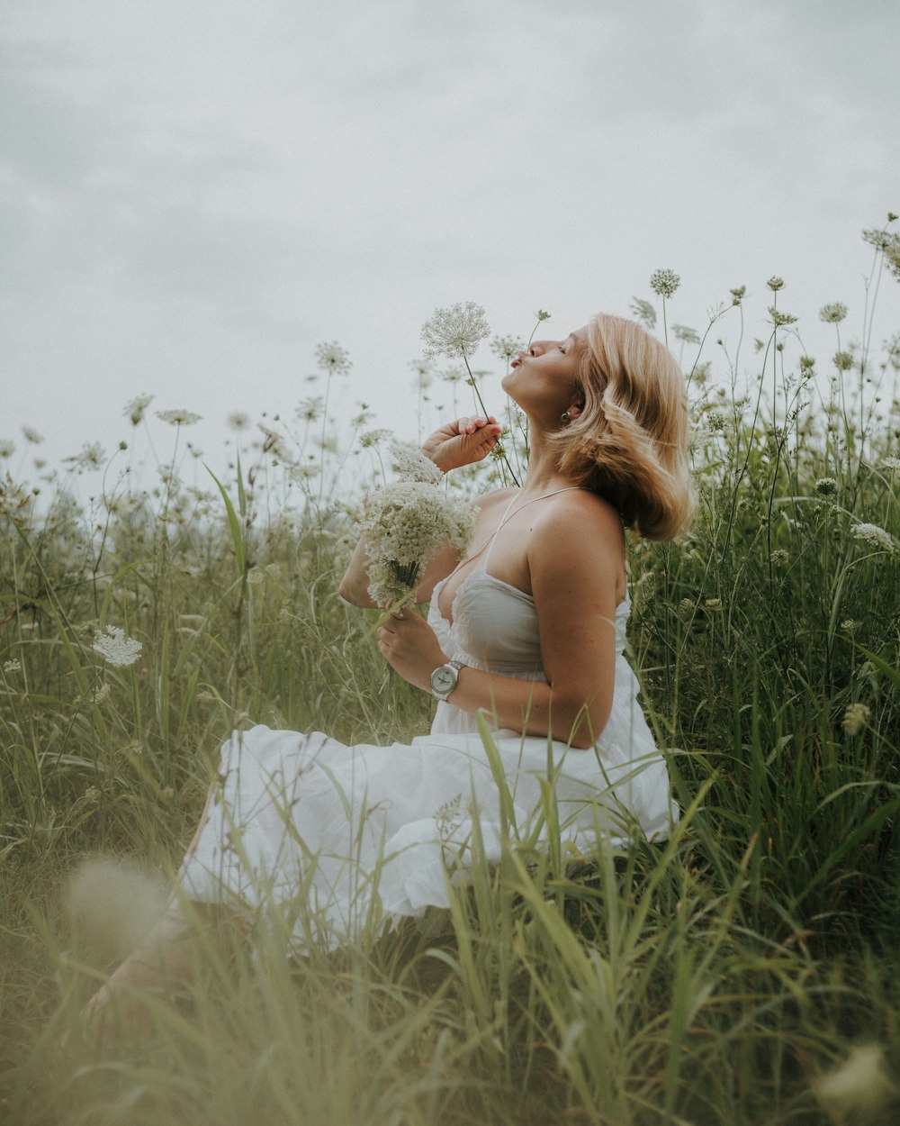 woman in white dress sitting on white flower field during daytime
