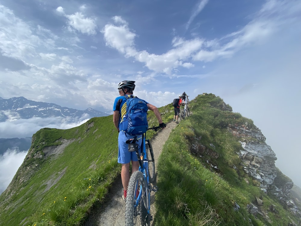 uomo in camicia blu e pantaloni neri che cavalca la bicicletta blu sul campo di erba verde durante il giorno