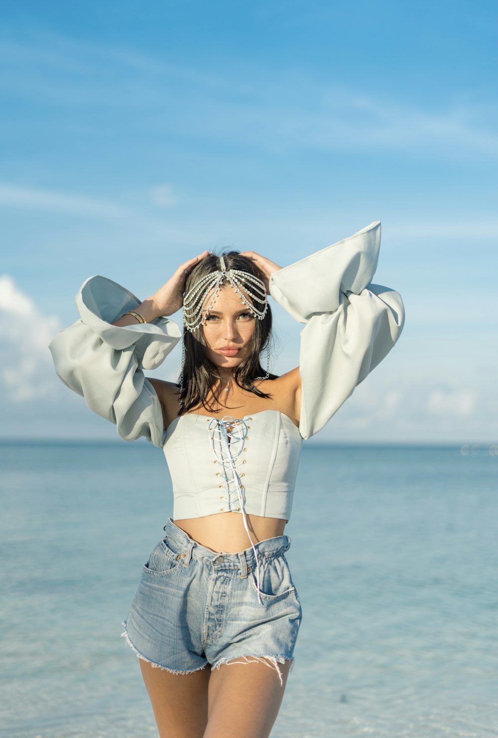 woman in white crop top and blue denim jeans standing on beach shore during daytime