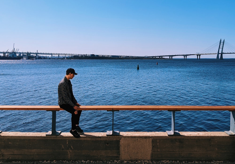 man in black shirt sitting on concrete bench near body of water during daytime