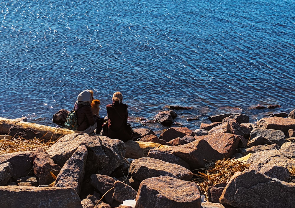3 Personen sitzen tagsüber auf Felsen in der Nähe von Gewässern