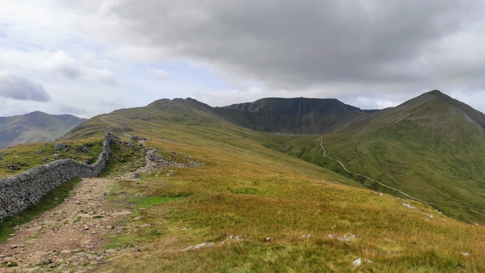 campo di erba verde vicino alla montagna sotto il cielo nuvoloso durante il giorno