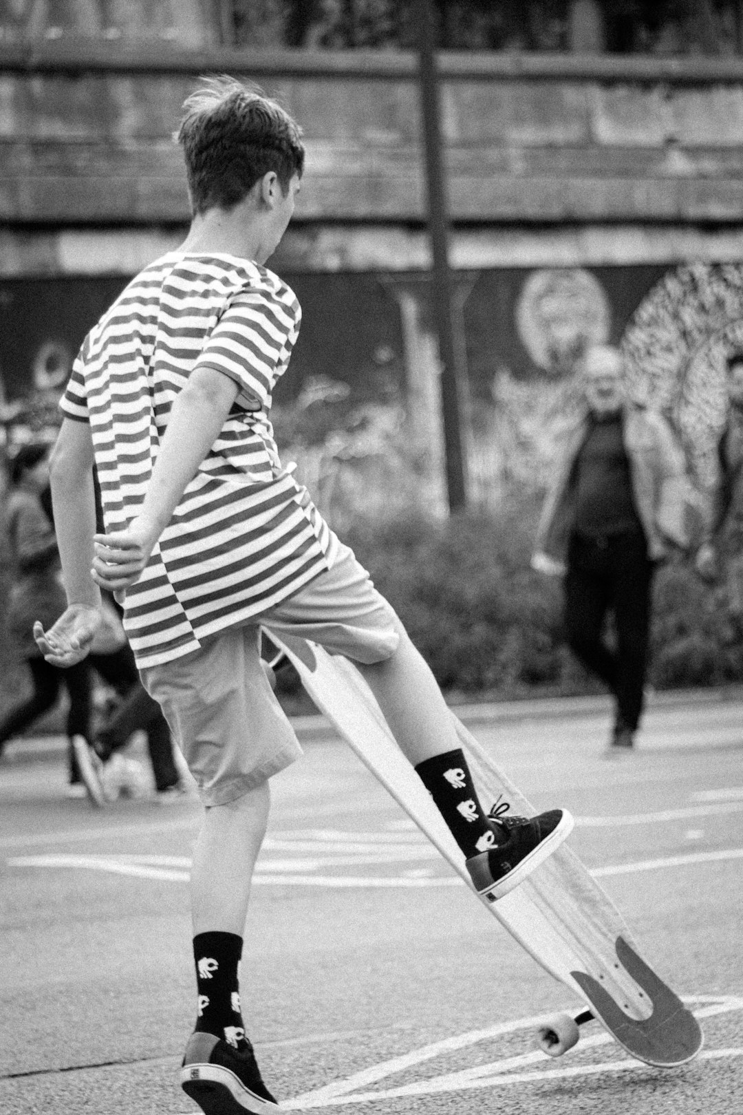 grayscale photo of man in striped shirt and shorts running on road