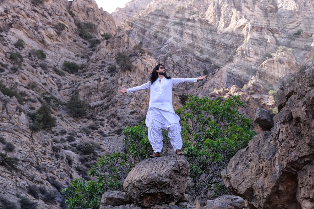 woman in white long sleeve shirt standing on brown rock