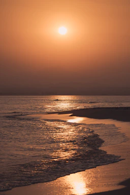 Eine helle, sonnendurchflutete Strandszene mit sanften Wellen und einem warmen Sonnenuntergangshimmel.