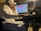 A person wearing a white shirt and a cap is intently focused on a computer screen with audio editing software. They are seated in a dimly lit room, wearing headphones, and appear to be engaged in music production.