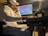 A person wearing a white shirt and a cap is intently focused on a computer screen with audio editing software. They are seated in a dimly lit room, wearing headphones, and appear to be engaged in music production.