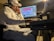 A person wearing a white shirt and a cap is intently focused on a computer screen with audio editing software. They are seated in a dimly lit room, wearing headphones, and appear to be engaged in music production.