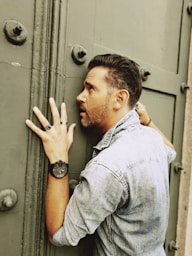 man in blue denim button up shirt leaning on gray metal door
