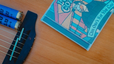 A close-up view of a guitar's bridge and strings alongside a colorful CD cover with a stained glass style illustration. The CD features text with musical notes on the guitar part.