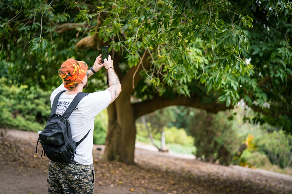 man in white dress shirt and black backpack standing near tree during daytime