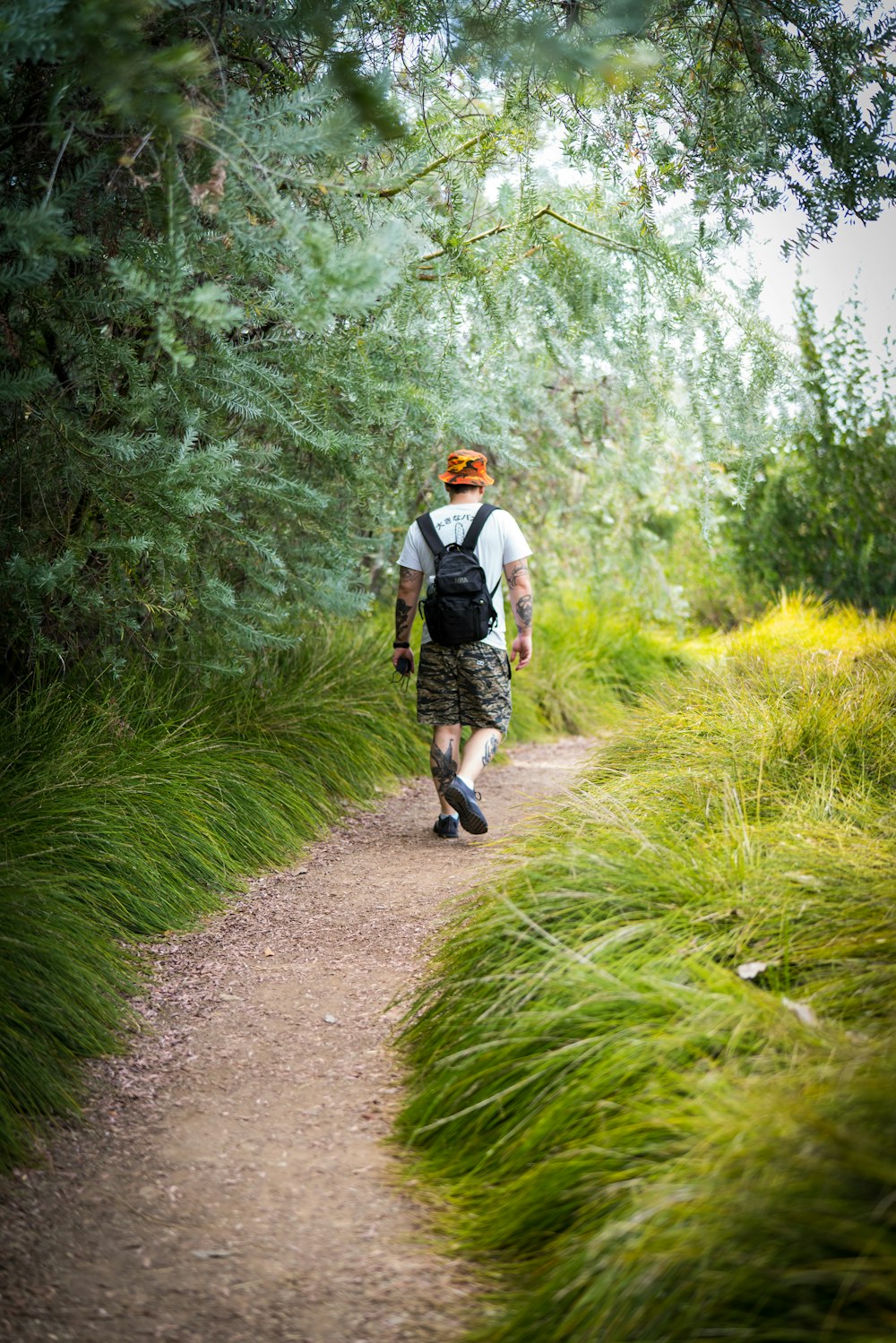 man in white shirt walking on dirt road between green grass during daytime