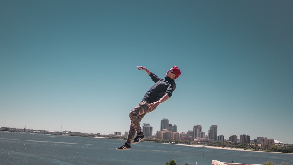 man in black jacket and brown pants jumping on mid air over looking city buildings during