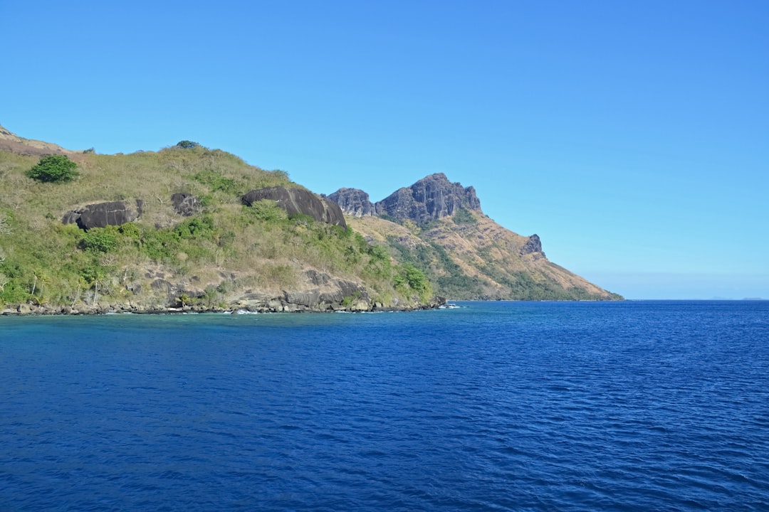 green and brown mountain beside blue sea under blue sky during daytime