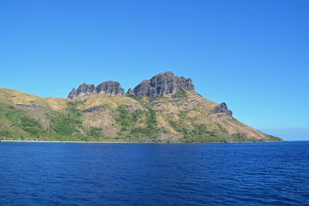 green and brown mountain beside blue sea under blue sky during daytime