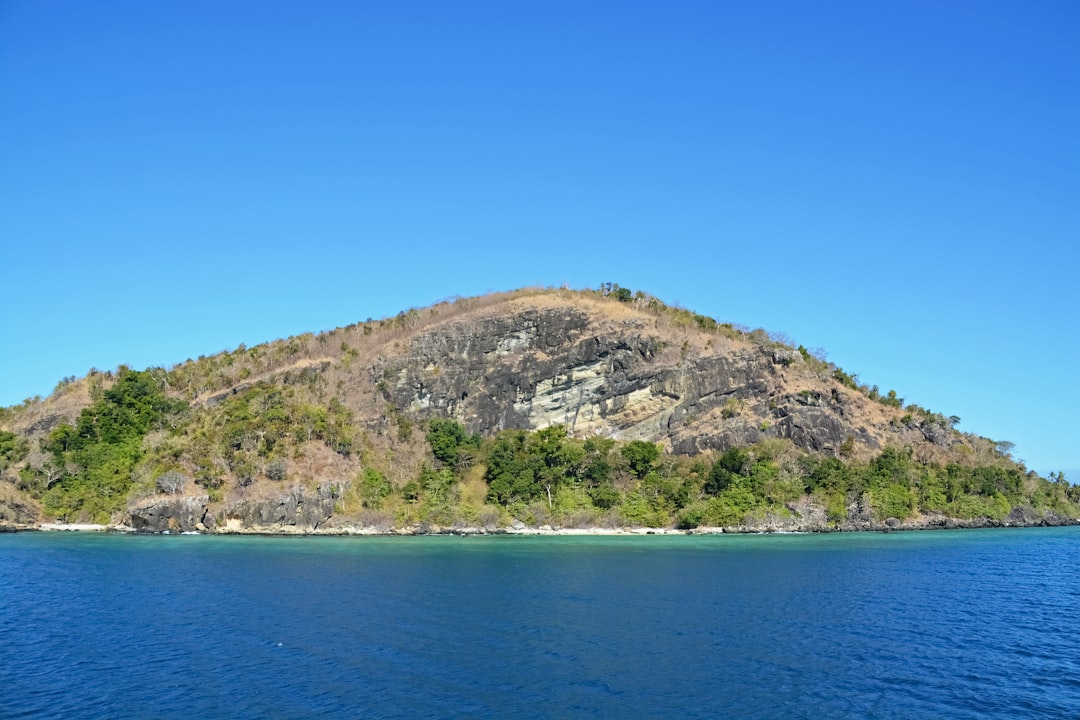 green and brown mountain beside blue sea under blue sky during daytime