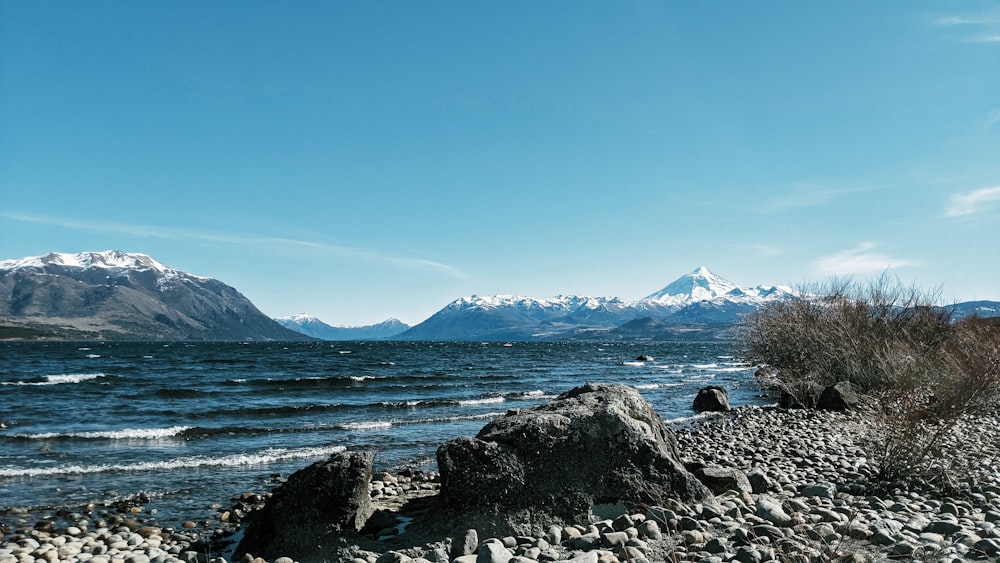 costa rocosa con montaña en distancia bajo el cielo azul durante el día