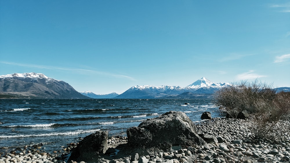 rocky shore with mountain in distance under blue sky during daytime