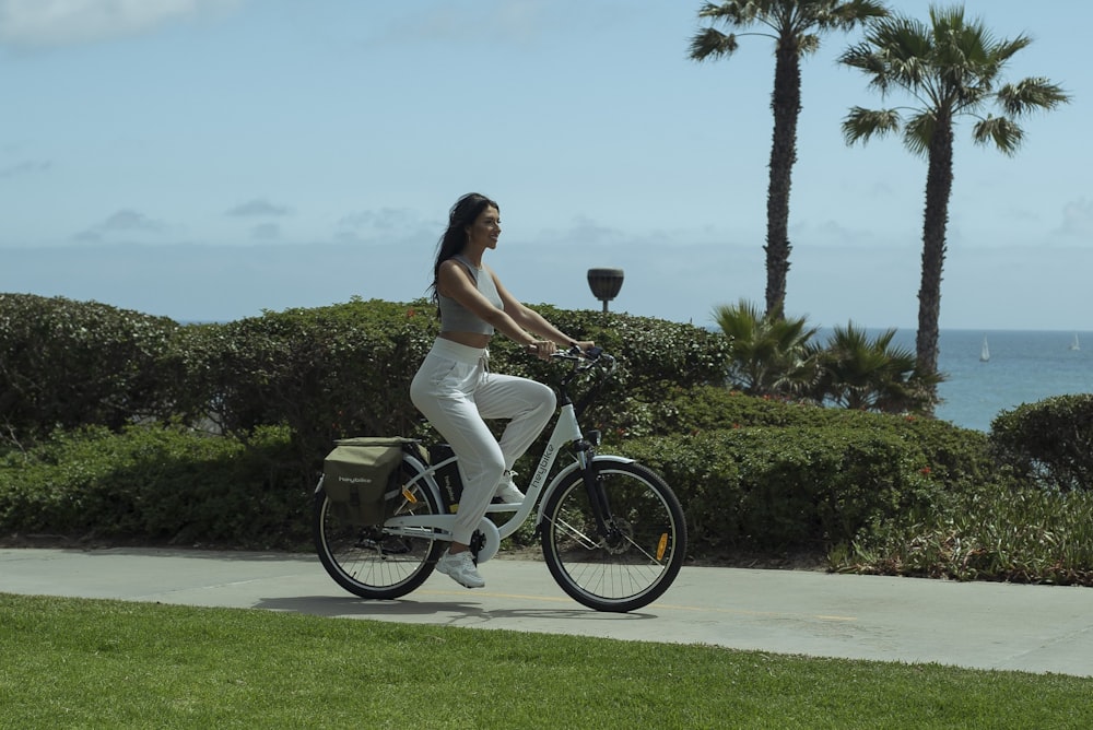 woman in white tank top and white pants riding on black bicycle during daytime