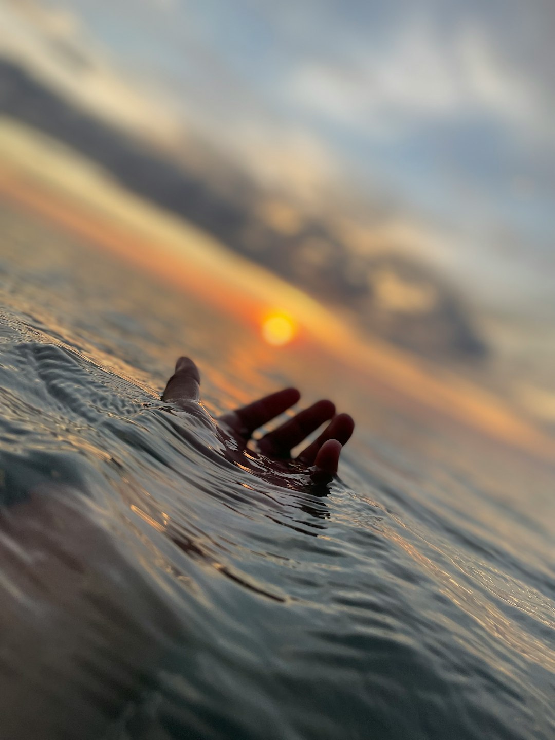 persons hand on water during sunset