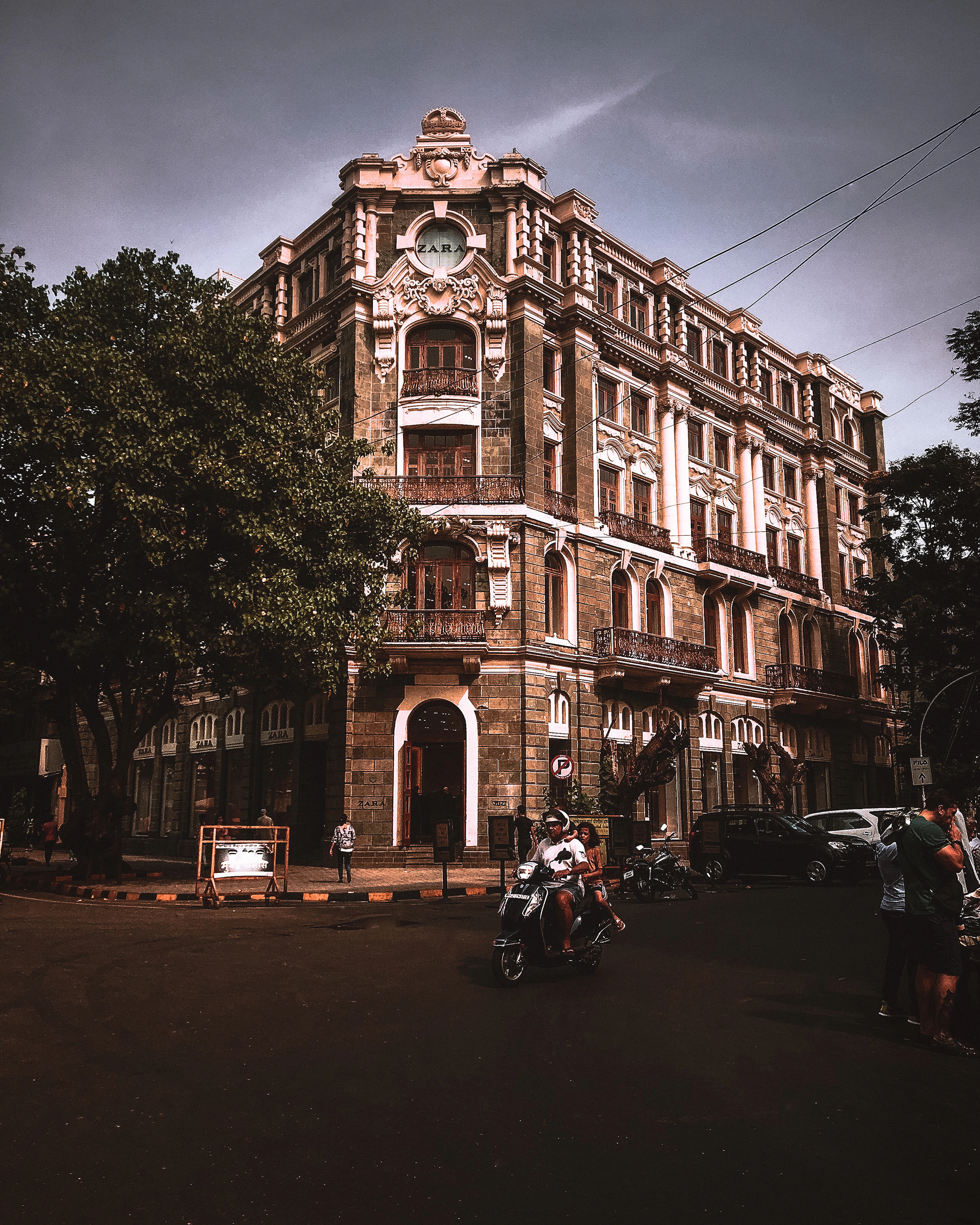 An ornate colonial-era building glows warmly against a darkening sky, with a motorbike passing below.