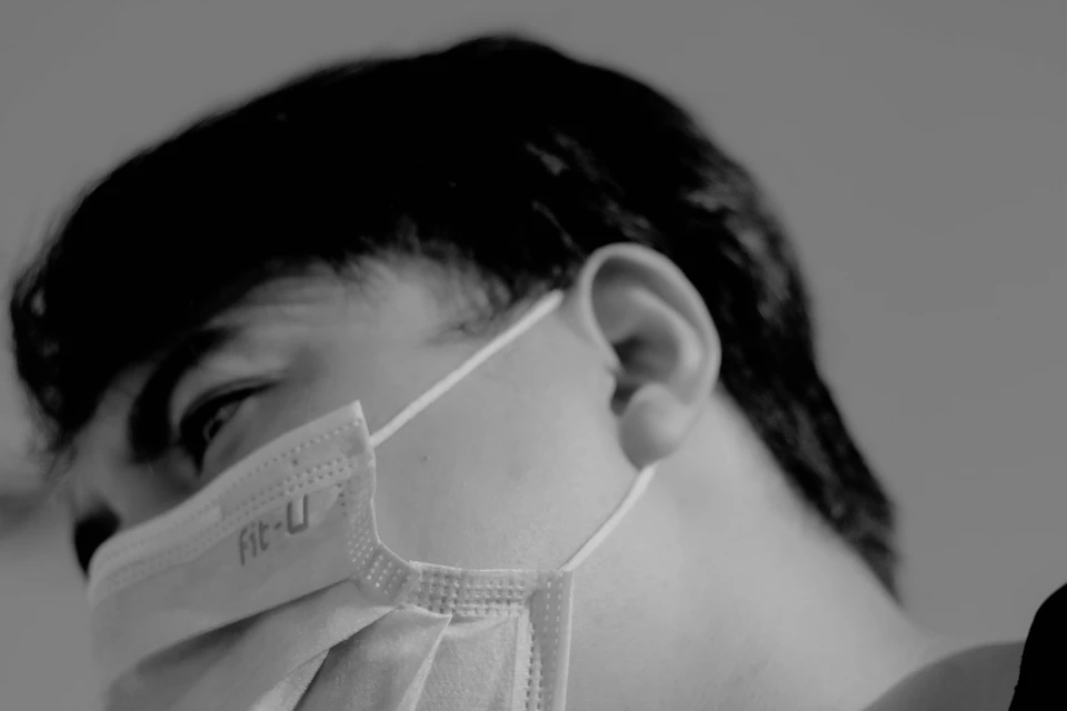 Person's face with head tilted, eyes closed, and worn white surgical mask covering nose and