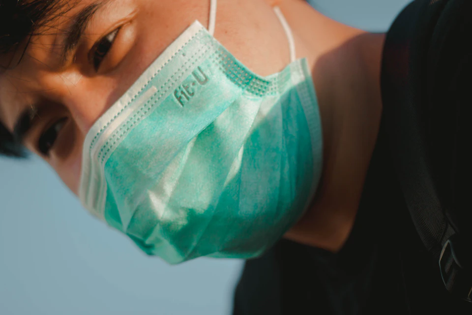 Person's face with eyes looking directly at camera, wearing green surgical mask outdoors