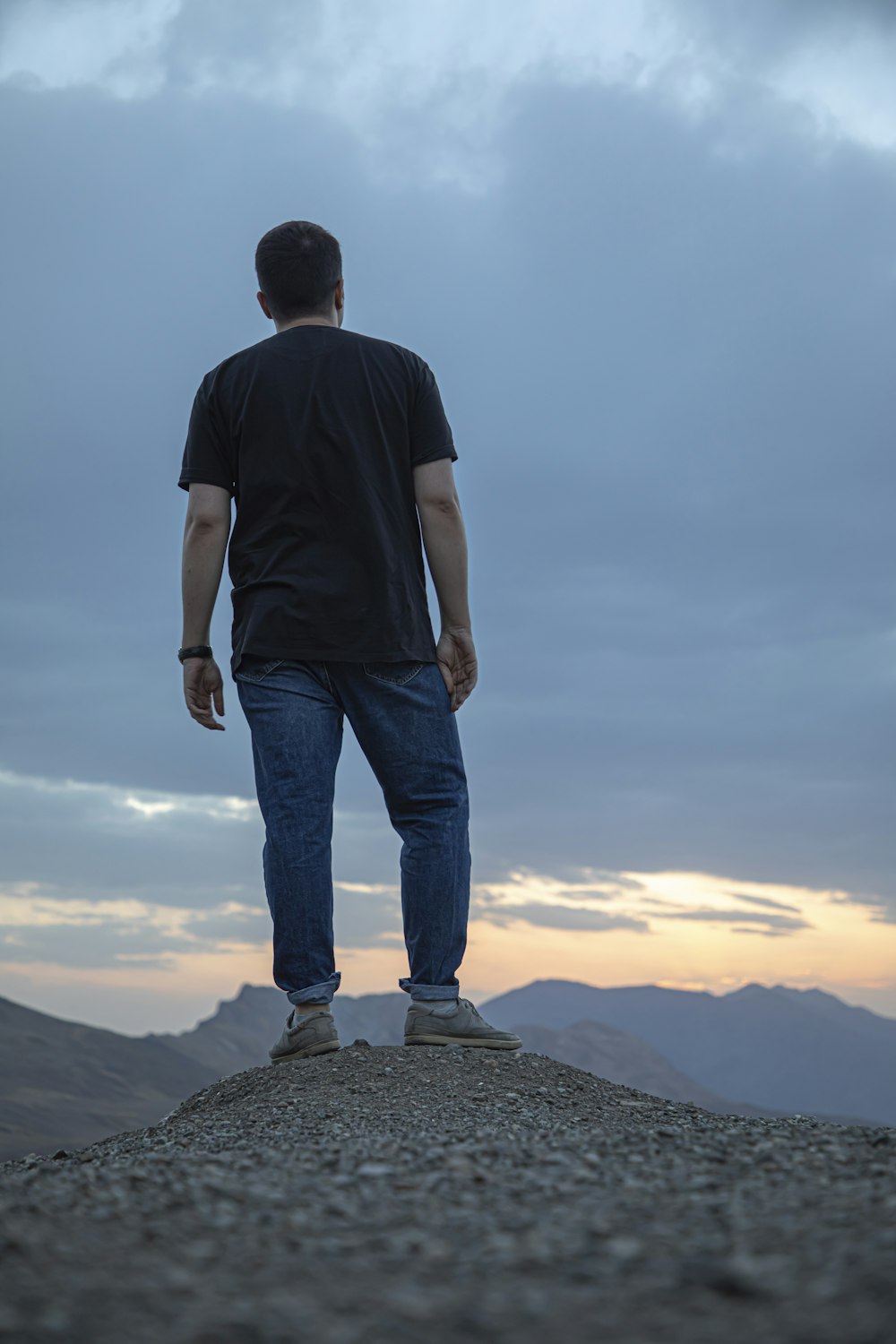 man in black t-shirt and blue denim jeans standing on rock formation during daytime