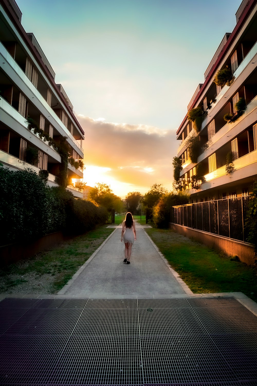 woman in white dress walking on pathway between buildings during daytime