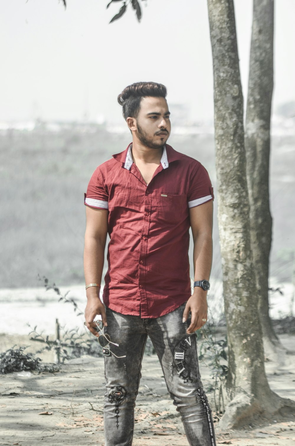 man in red polo shirt and blue denim jeans standing beside tree