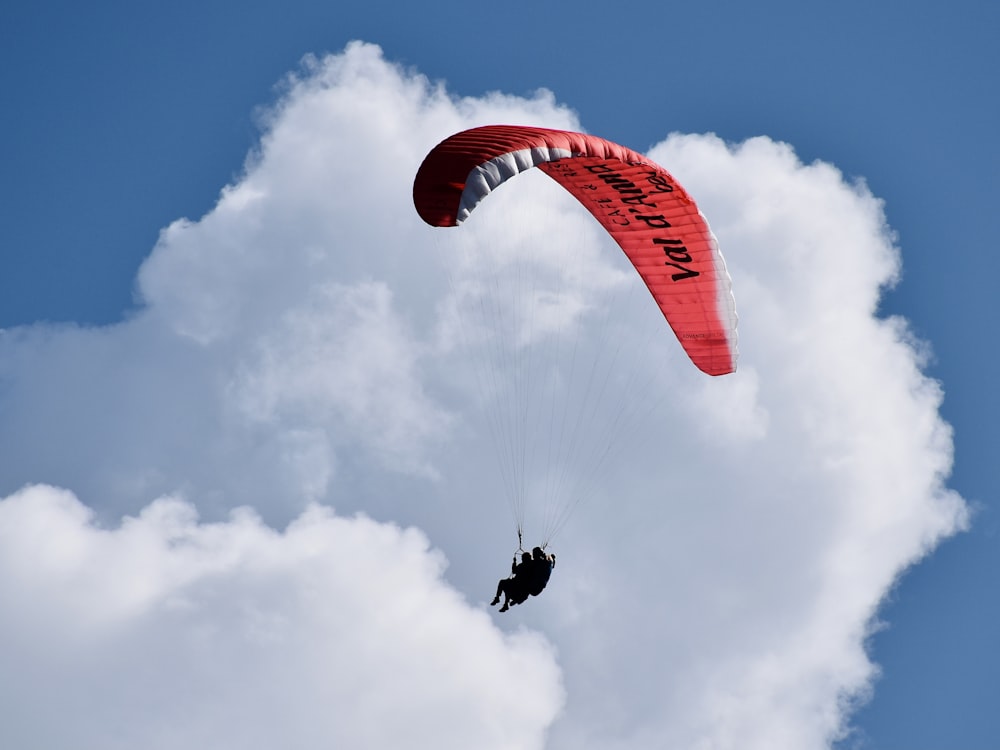 Person, die tagsüber auf einem roten und weißen Fallschirm unter weißen Wolken und blauem Himmel reitet