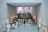 A modern museum interior features smooth concrete walls with quadratic perforations and a reflective glass floor. Ancient artifacts and sculptures are displayed on both sides. Visitors walk and observe the exhibits, with a staircase leading to an upper level in the background.