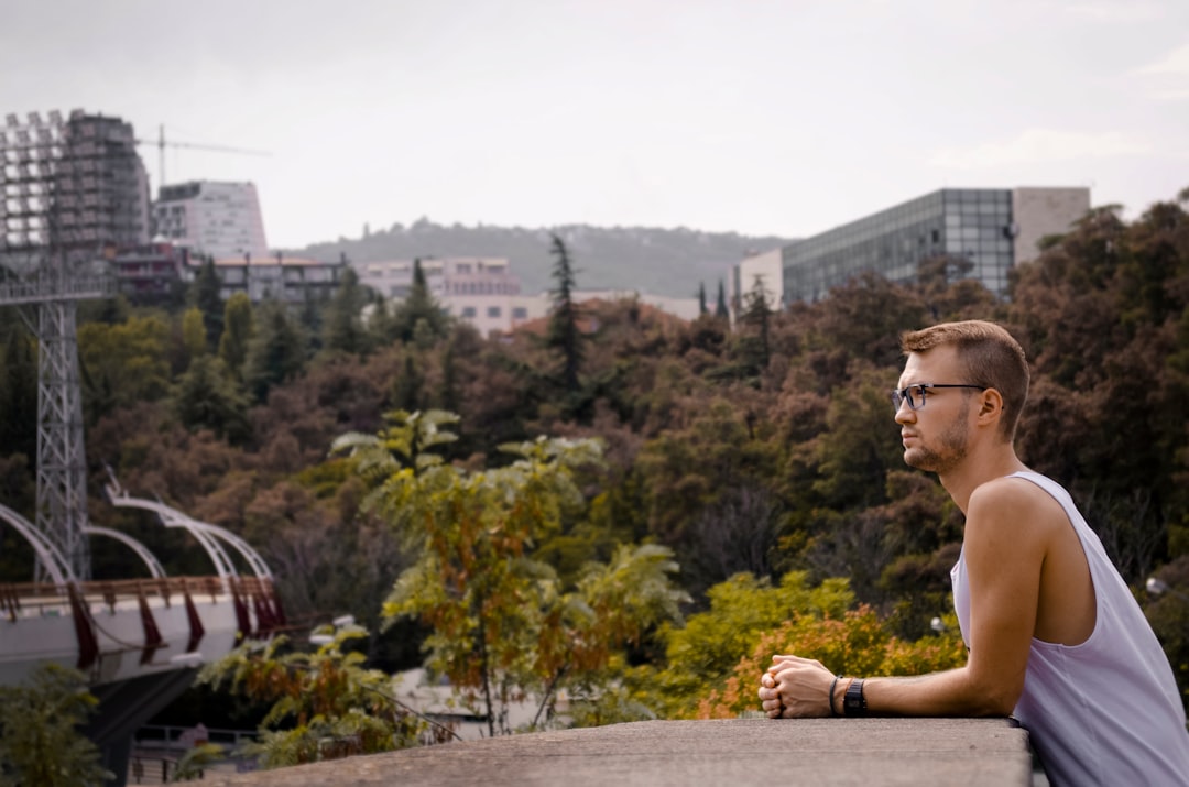 man in white tank top wearing eyeglasses sitting on brown wooden bench during daytime