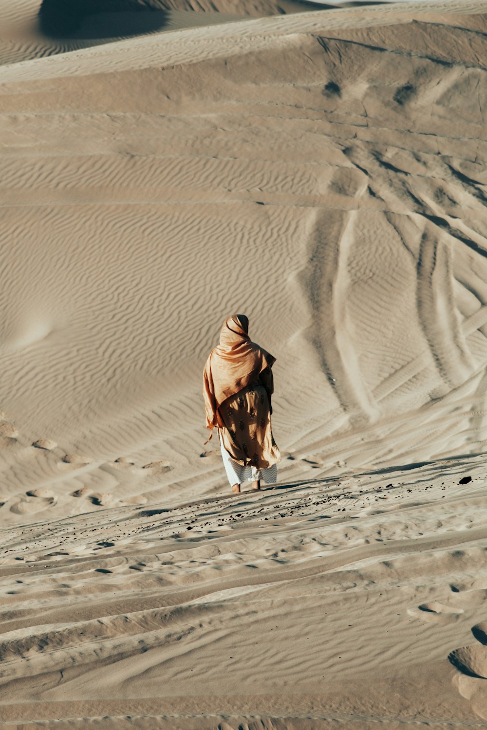 Persona con chaqueta marrón caminando sobre la arena durante el día