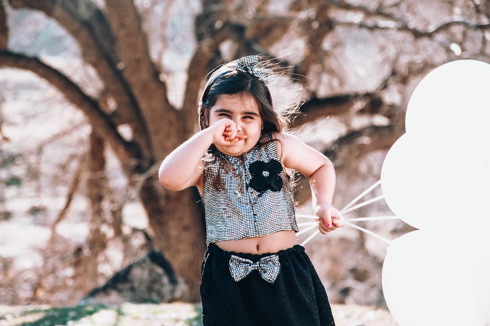 girl in black and white polka dot sleeveless dress holding white balloons