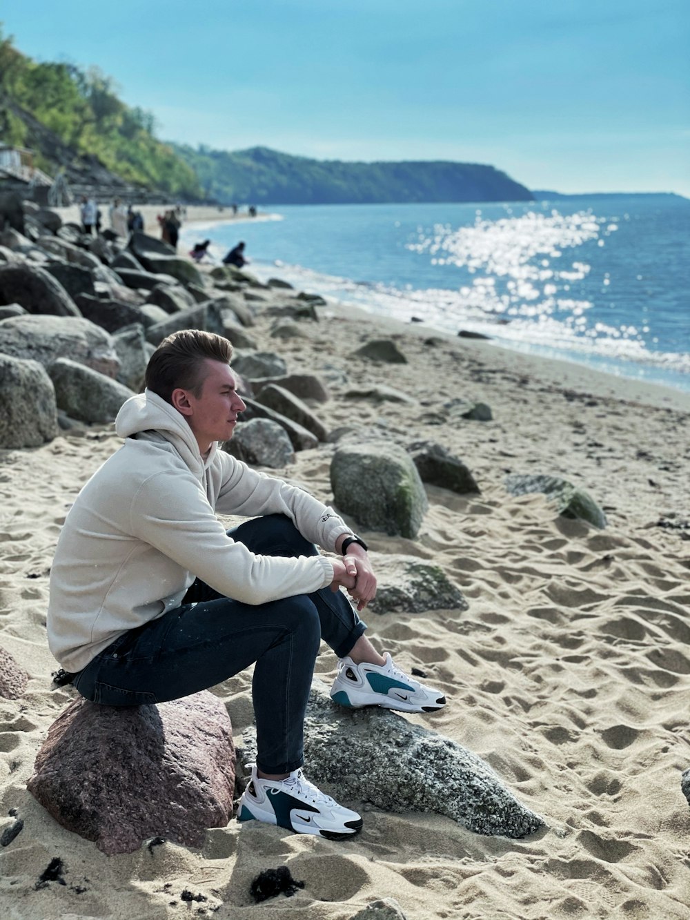 man in gray hoodie and blue denim jeans sitting on rock near body of water during