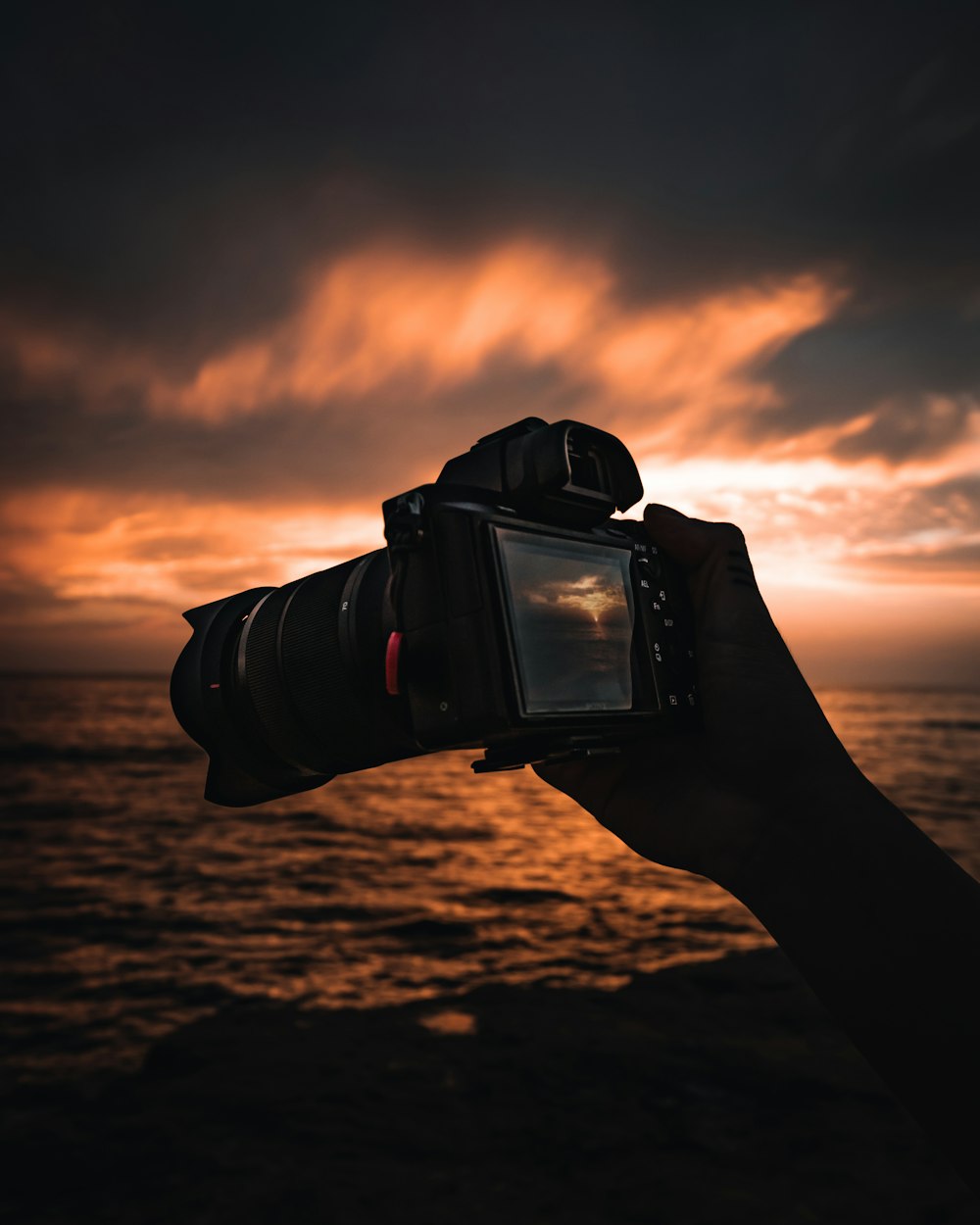 Personne tenant un appareil photo reflex numérique noir au coucher du soleil